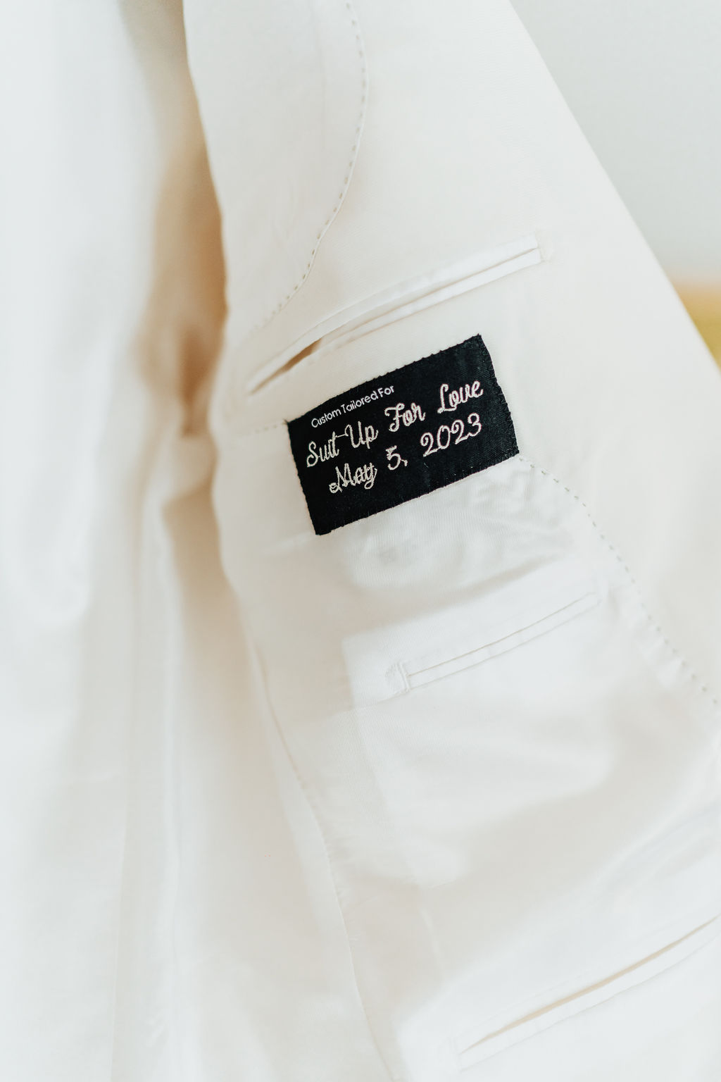Inside of white suit jacket with embroidery "Suit up for Love, May 5, 2023."