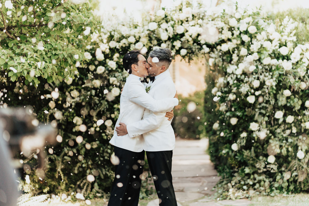 Isaac (left) and Joe (right) sharing their first kiss in front of floral arch.