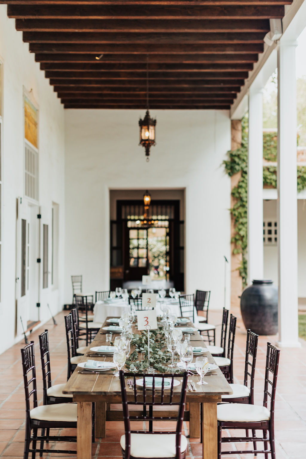 Long wood table with dinner settings and greenery on patio with red tile floors and wood ceiling