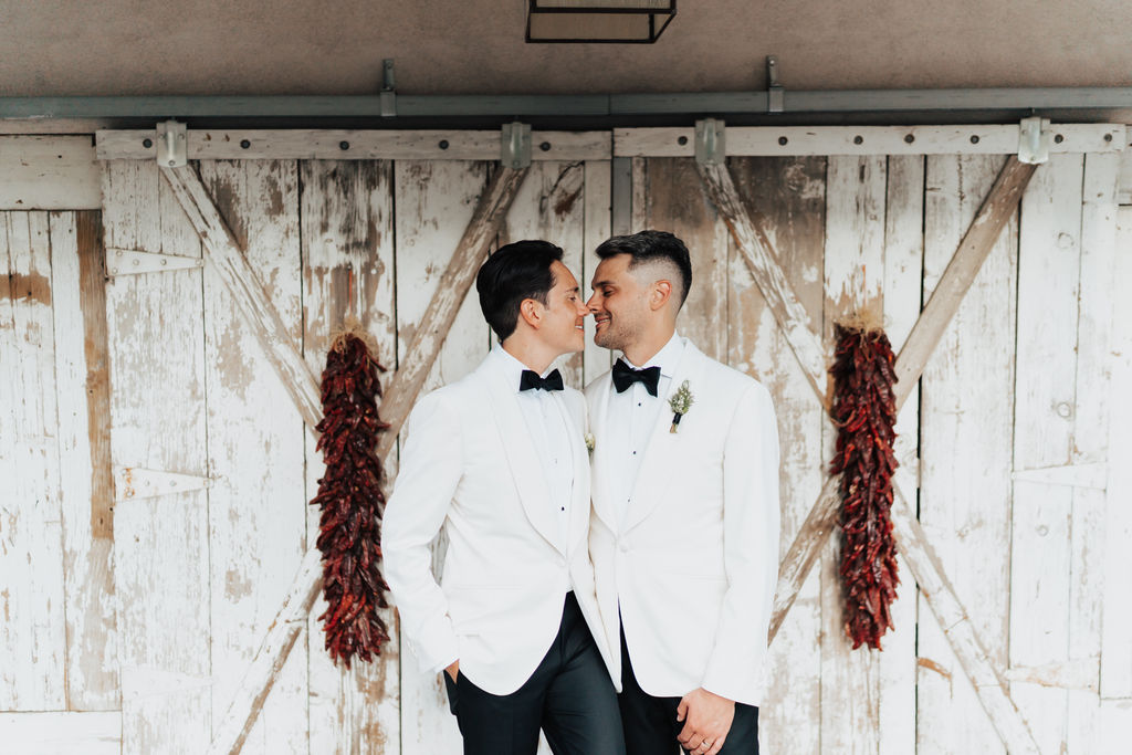 Isaac (left) and Joe (right) standing in front of wooden barn doors lined with ristras on each side.